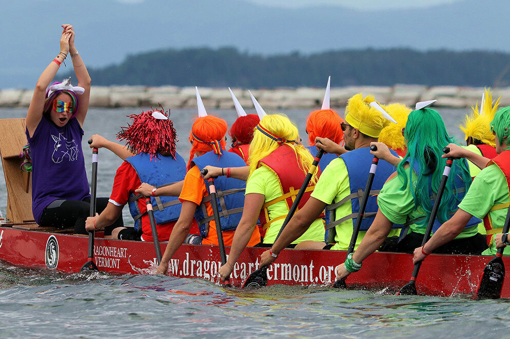 A colorful dragon boat team celebrates and paddles on the water during a competition.