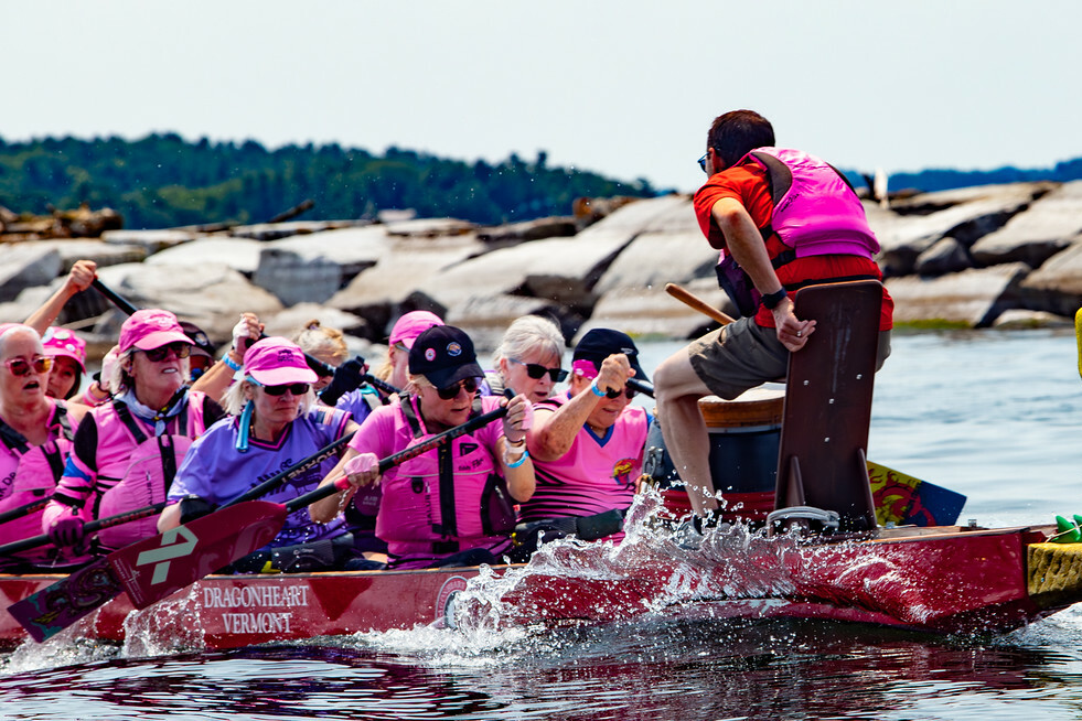 Women in pink shirts and life jackets paddling a dragon boat on the water.