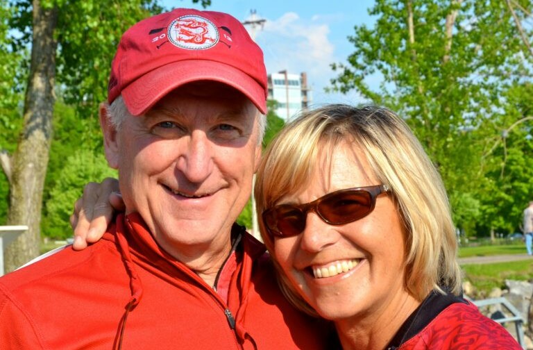 Linda and John Dyer posing together outdoors in matching red attire.