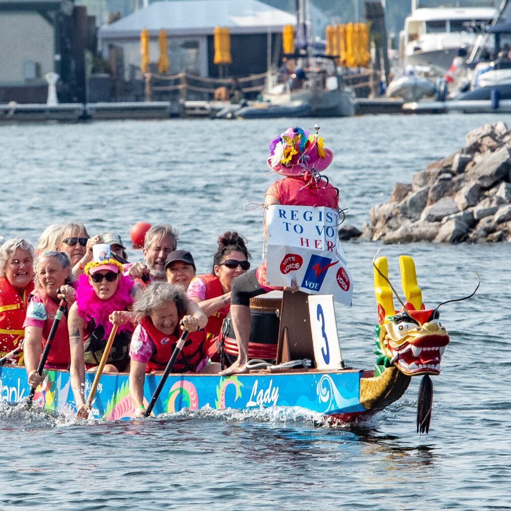 Dragon boat team with women paddling and a "Register to Vote" sign on the boat.