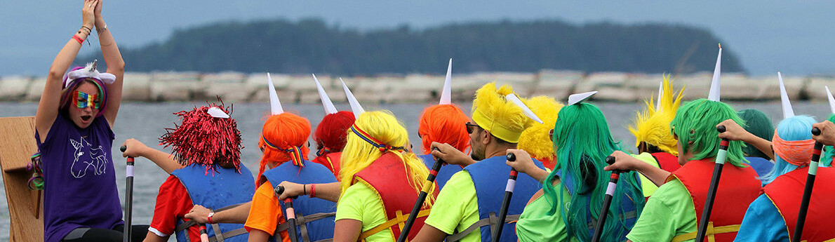 A team in colorful costumes prepares to race in dragon boats on a lake.