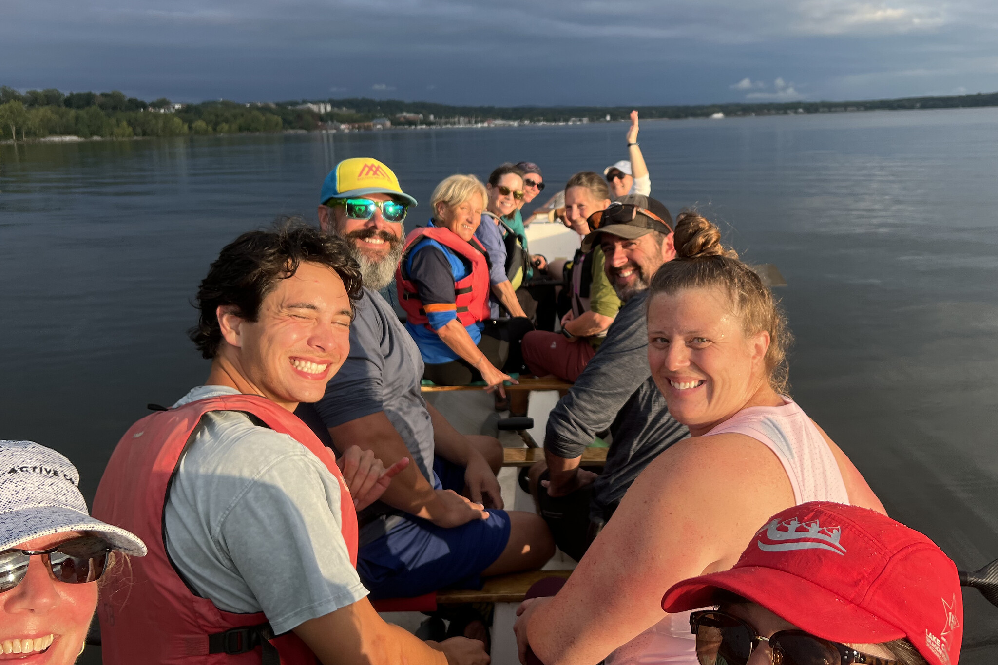 A group of people smiling while seated in a canoe on a calm body of water.