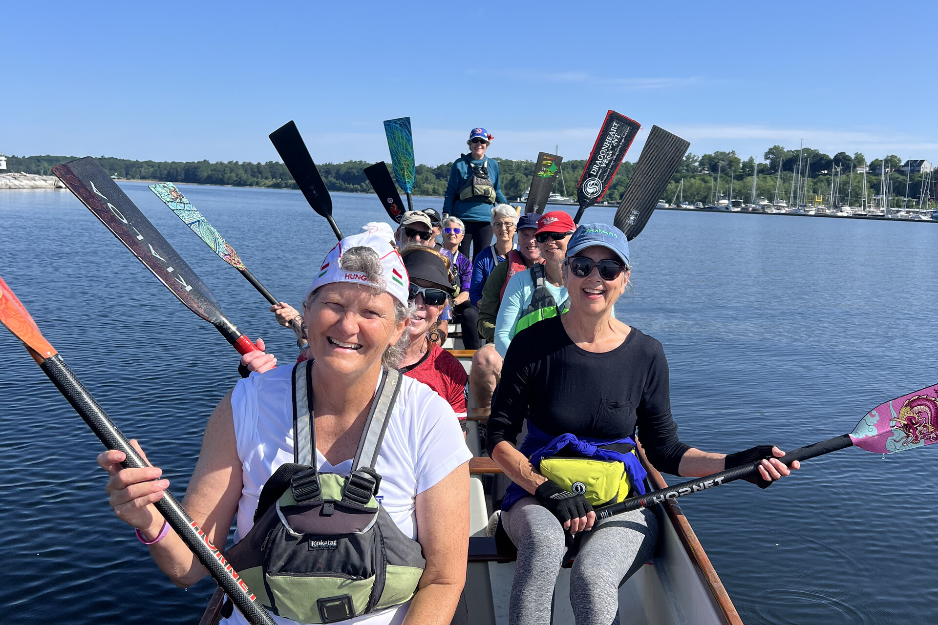Group of women smiling and paddling in a canoe on a sunny day.